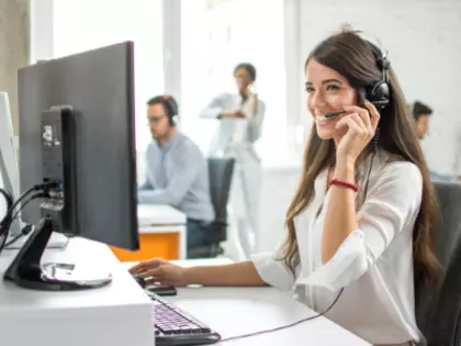Frau, die mit Headset telefonier vor einem Bildschirm
