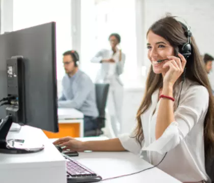 Frau, die mit Headset telefonier vor einem Bildschirm